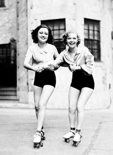 Two young women in black shorts roller-skating down a street