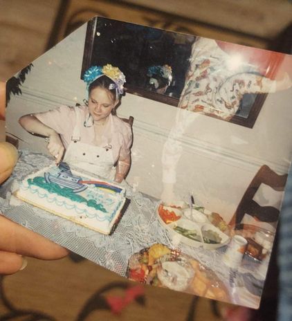 A young woman in a party hat made of gift bows cuts a cake